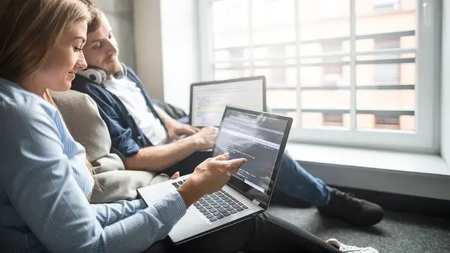 Two web developers collaborating on laptops while reviewing code and server configuration, illustrating teamwork involved in setting up secure and reliable hosting and domain services.