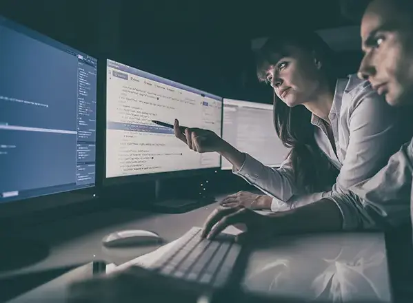 Two developers collaborating at a desk, reviewing code on multiple monitors during a custom web application development session