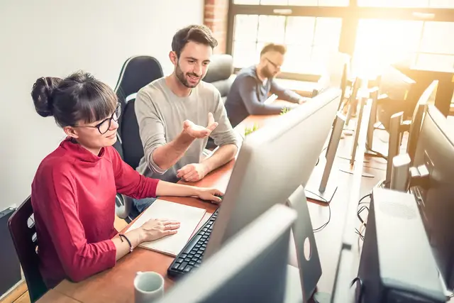 Team of web designers collaborating at a desk with large monitors in a bright modern office, discussing ecommerce website layout and performance optimisation.