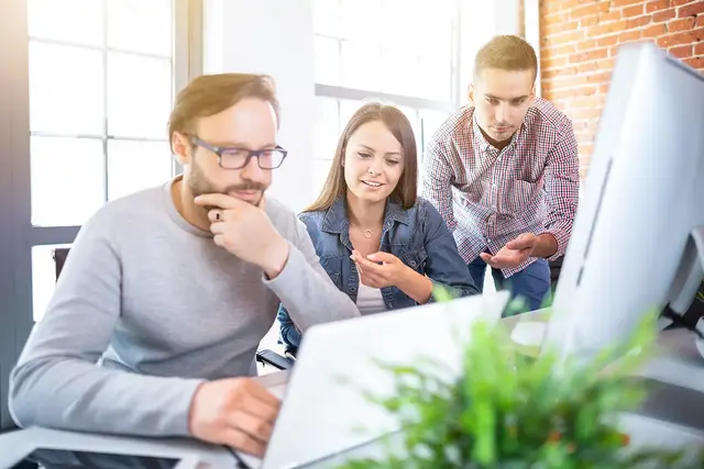 Web design team collaborating in a modern office, reviewing a responsive website layout on a desktop monitor, symbolising teamwork, UX strategy, and digital project planning.