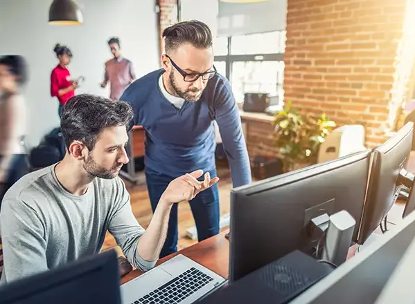 Two web developers collaborating in a modern office, reviewing a website technical audit on dual monitors.