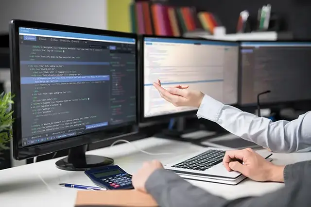 Developer working on a multi-monitor setup, writing and debugging HTML and CSS code in a collaborative environment. Ideal visual for illustrating modern website development, frontend and backend integration, and team-based coding practices.
