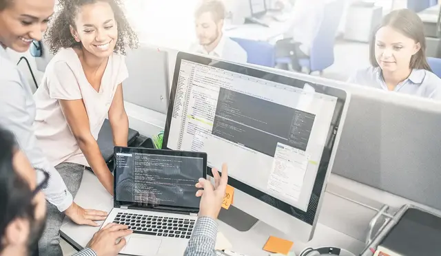 Team of SEO professionals collaborating at a workstation with code displayed on a large monitor and laptop, representing technical analysis during an SEO audit.