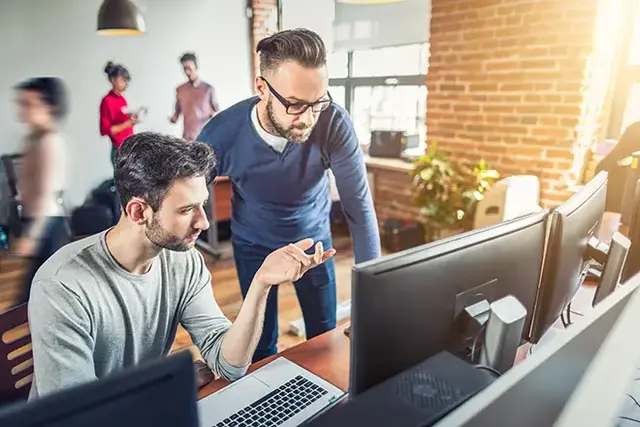 Two web developers collaborating in a modern office, reviewing a website technical audit on dual monitors.