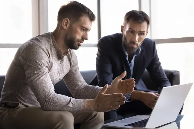Two professional men having a focused discussion while reviewing SEO strategy on a laptop during an SEO consultancy meeting.