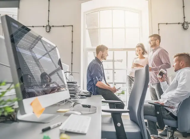 Team of digital marketing professionals collaborating in a modern office with coding displayed on a computer screen in the foreground.