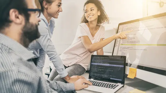 Team of digital marketing professionals collaborating around a desktop and laptop, reviewing website code and discussing off-page SEO strategy and implementation.