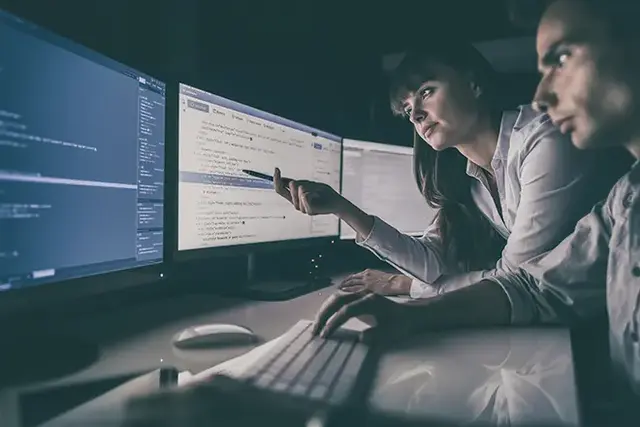 Two developers collaborating at a desk, reviewing code on multiple monitors during a custom web application development session