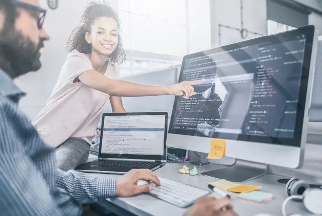 Team collaboration in a modern office setting with two colleagues working on content-related code and strategy, highlighting digital content workflow, CMS implementation, and the technical execution side of content marketing.