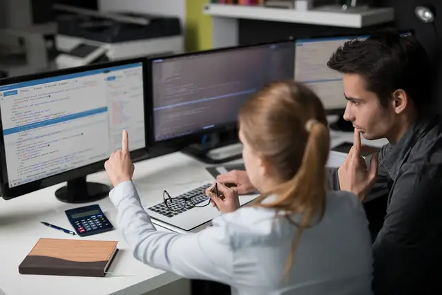 Web developers analysing code across multiple screens during a website maintenance and troubleshooting session, focusing on performance and security fixes.