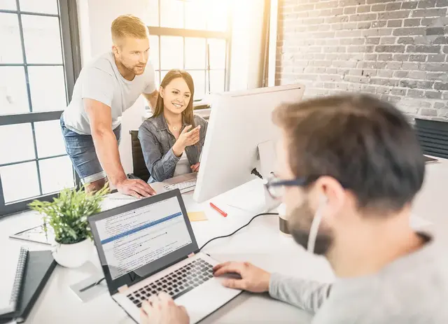 Team of digital marketers collaborating in a modern office, reviewing local SEO strategy on a desktop monitor, with code displayed on a laptop in the foreground.