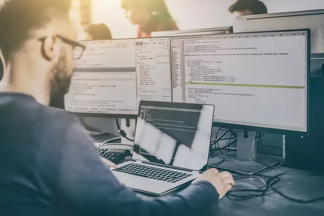 A programmer intently focuses on coding, with a computer screen displaying Bing's Ad Management features. The workspace hints at digital marketing and software development tasks in progress.