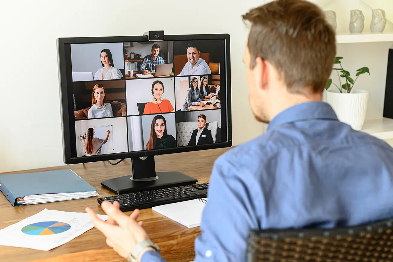 Person participating in an online team video call with eight colleagues displayed on the monitor.
