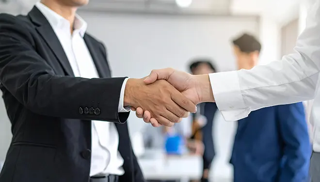 Two business professionals shaking hands in an office, representing trust, partnership and a positive working relationship